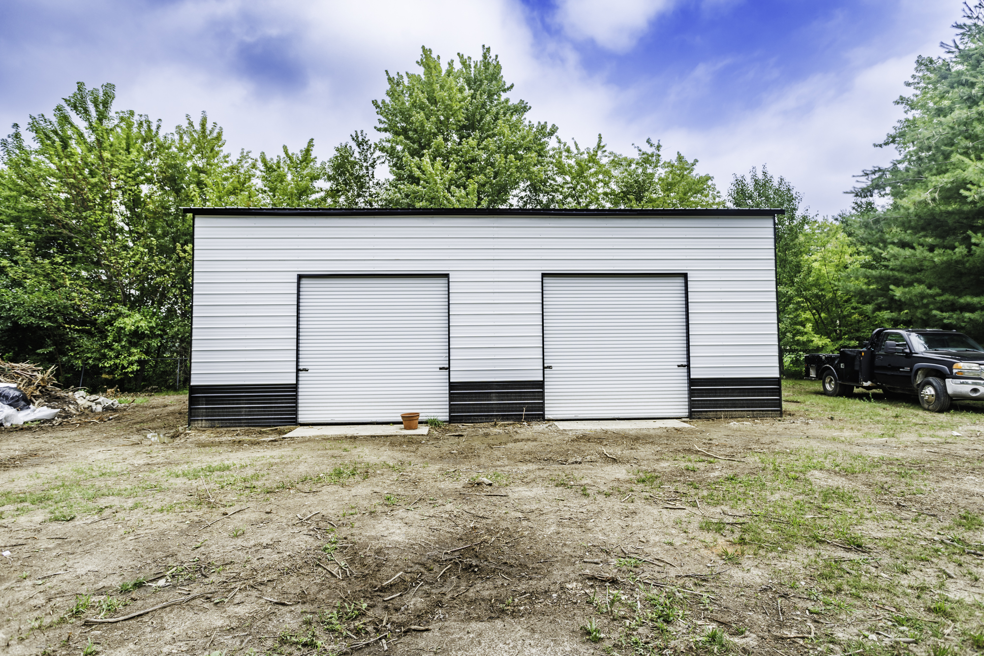 Steel garage with charcoal siding and red trim next to residential home