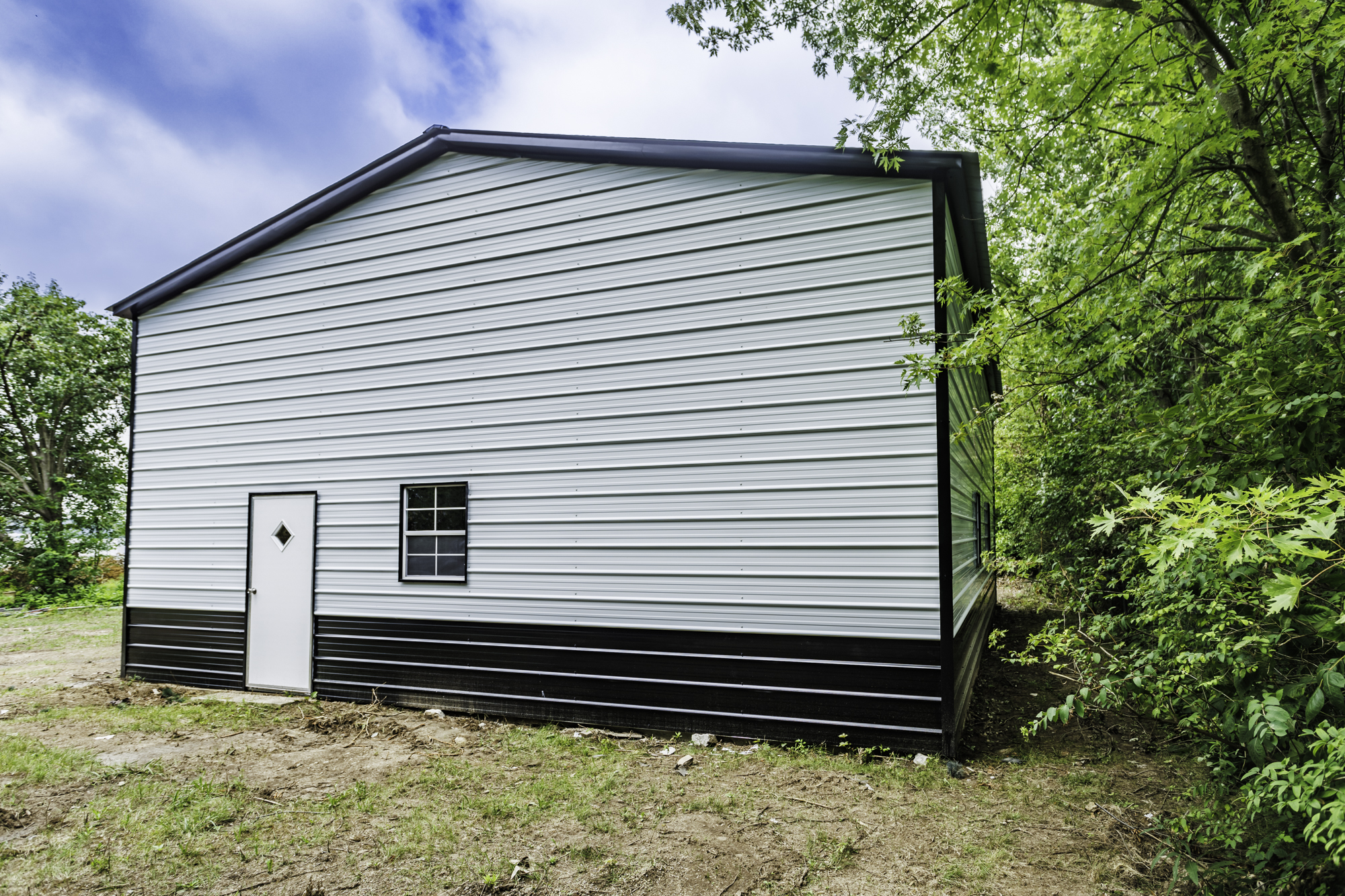 Barn red steel garage on open farmland with white trim and roll-up door